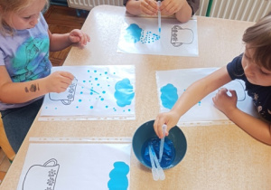Dzieci przy stoliku robią kropki z kolorowej wody na kartce