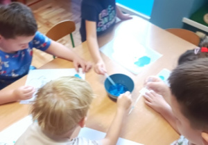 Dzieci przy stoliku robią kropki z kolorowej wody na kartce