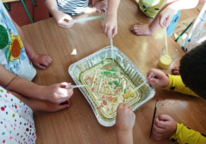 Dzieci stoją wokół stolika i zakraplają kolorowe mleko do kuwety z olejem