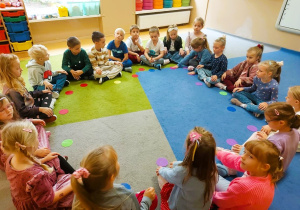 Dzieci siedzą na dywanie trzymając kolorowe kropki