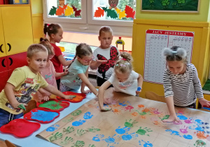Dzieci odbijają na papierze dłonie pomalowane farbą