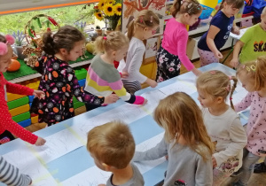 Dzieci chodzą do okoła stołu i rysują w rytm melodii
