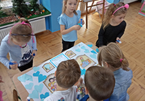 Dzieci wyklejają papierowe serduszka na plakacie