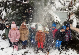 Dzieci stoją pod drzewem, z którego spada śnieg