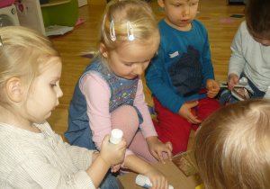Dzieci przyklejają srebrne kawałki folii do pudełka