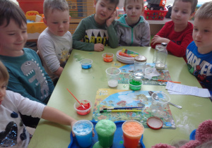 Dzieci obserwują wynik doświadczenia jak pod wpływem połączenia wody, sody i kwasku cytrynowego, płyn zaczyna podnosić się, burzyć i uciekać z pojemnika