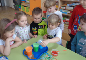 Dziewczynka wsypuje do kolorowej wody kwasek cytrynowy