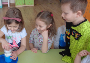 Do rozrobionej z farbą wody dziecko wkłada do słoika kawałek waty, ugniata i wsypuje brokat
