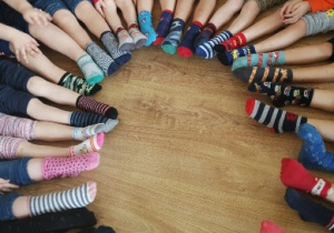 Dzieci siedzą w kole i pokazują kolorowe, różnorodne skarpetki na nogach