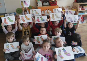 Przedszkolaki prezentują prace plastyczne przedstawiające dwie kolorowe skarpetki