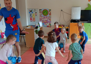 Dzieci chodzą trzymając piłki między nogami