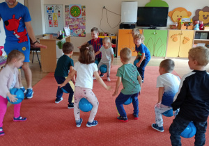 Dzieci chodzą trzymając piłki między nogami