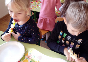 Dzieci jedzą wykonane szaszłyki z owoców