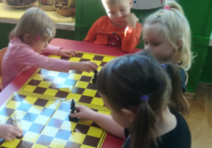 Przedszkolaki przesuwają po szachownicy figurę króla w pokazany sposób