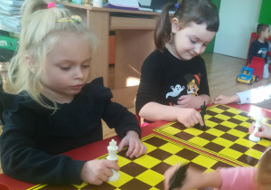 Przedszkolaki przesuwają po szachownicy figurę króla w pokazany sposób