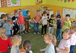 Dzieci stojąc w kręgu podają sobie dynie.