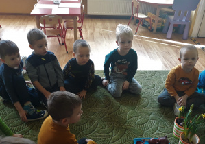 Dzieci siedzą na dywanie w czasie zajęcia edukacyjnego