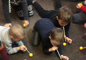 Dzieci dmuchają powietrze przez słomki i wprawiają piłeczki pingpongowe w ruch