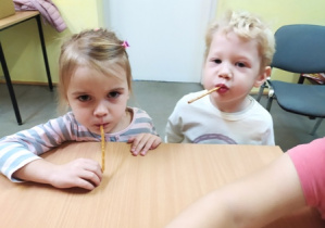 Dzieci zjadają paluszki bez użycia rąk.