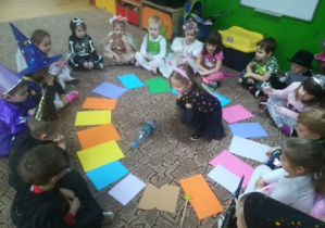 Dzieci siedzą w kole przed kolorowymi kartkami