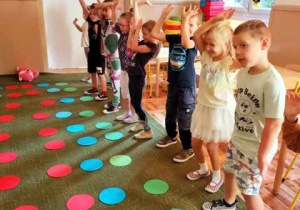 Dzieci stoją przez szeregami ułożonych na dywanie kolorowych kół