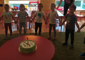 Dzieci stoją wokół stoliczka, na którym stoi tort