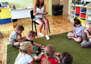 Dzieci siedzą na dywanie i słuchają czytanej bajki