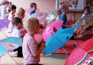 Dzieci siedzą za parasolkami