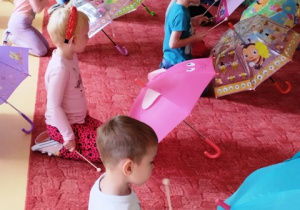 Dzieci wystukują rytm pałeczkami na parasolkach