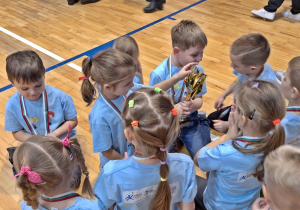 Rozemocjonowane dzieci ogladają puchar i medale zdobyte na Zduńskowolskich Igrzyskach Przedszkolaków