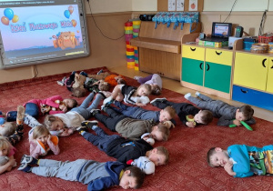 Dzieci odpoczywają na dywanie ze swoimi misiami i innymi przytulamnkami