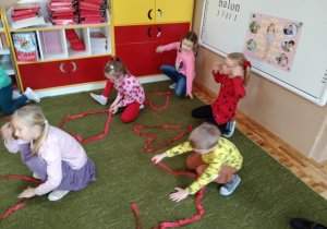 Dzieci układają kształt serca z czerwonej wstążki