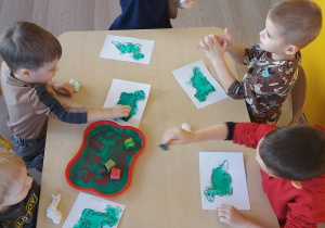 Dzieci stemplują gąbką umoczona w farbie kontur dinozaura