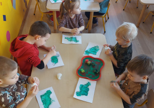 Dzieci stemplują gąbką umoczoną w farbie kontur dinozaura