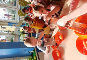 Dzieci ścierają marchewkę i jabłka na tarkach
