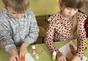 Dzieci wyklejają kontur marchewki pomarańczowym papierem