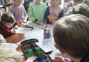 Dzieci siedzą przy wspólnym stole i kolorują obrazki