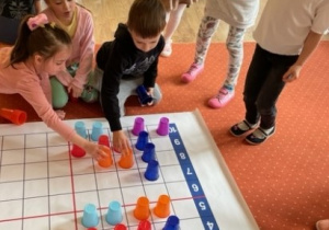 Dzieci układają kolorowe kubki na macie według instrukcji