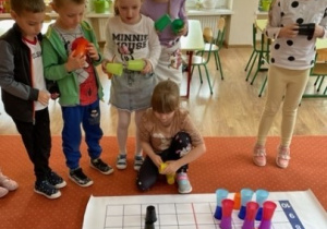Dzieci układają kolorowe kubki na macie według instrukcji
