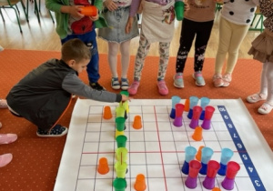 Dzieci układają kolorowe kubki na macie do kodowania