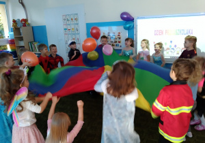 Dzieci uczestniczą w zabawie z chusta animacyjną i balonami