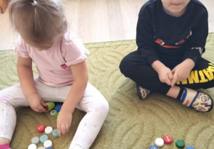 Dzieci układają plastikowe kropki na dywanie