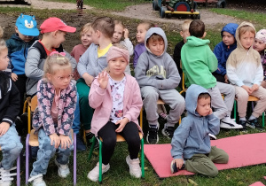Dzieci siedzą na krzesełkach w ogrodzie przedszkolnym