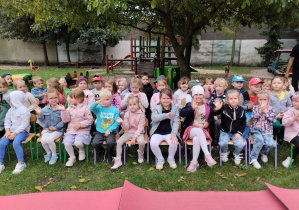 Dzieci siedzą na krzesełkach w ogrodzie przedszkolnym