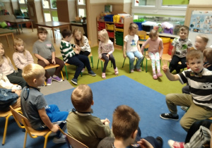 Dzieci siedzą w kole na krzesłach