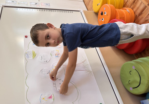 Chłopiec przykleja na szablon drzewa narysowany przez niego talent