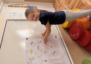 Dziewczynka przykleja na szablon drzewa narysowanych przez nią talent