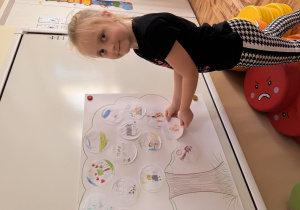 Dziewczynka przykleja na szablon drzewa narysowanych przez nią talent