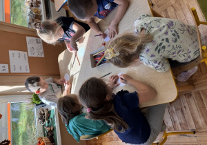 Dzieci siedzą przy stoliku i rysują kredkami