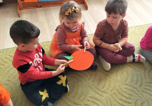 Dzieci podają sobie papierową dynię klamerkami